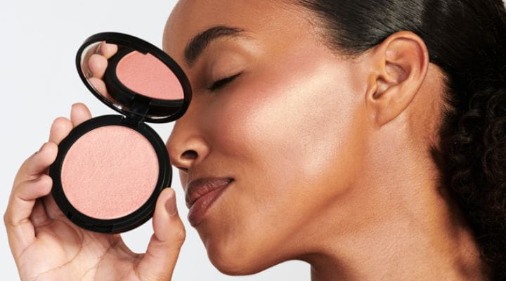 Modelo segurando blush facial rosa e exibindo efeito na maquiagem