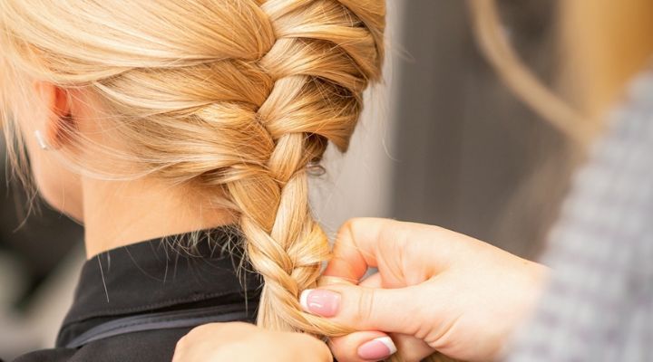 Cabeleireira finalizando trança em modelo de cabelo loiro