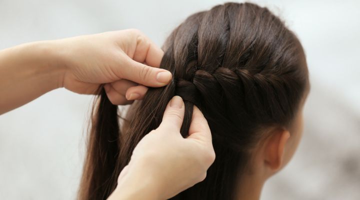 Cabeleireira fazendo trança embutida em modelo com cabelo castanho