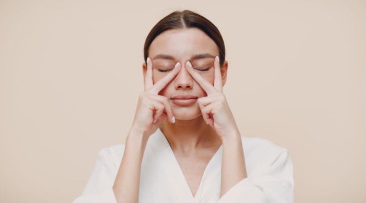 Foto de uma modelo realizando o movimento beija-flor do yoga facial com as mãos no canto dos olhos.