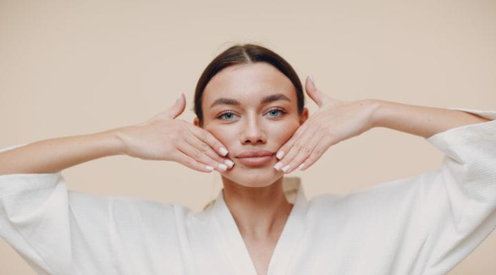 Foto de uma modelo fazendo yoga facial com as mãos nas bochechas.