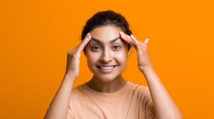 Foto de uma modelo realizando o movimento girassol do yoga facial com as mãos em seus sobrancelhas.