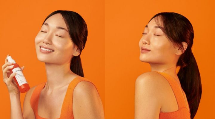 Foto da modelo aplicando a bruma facial de vitamina C em seu rosto.