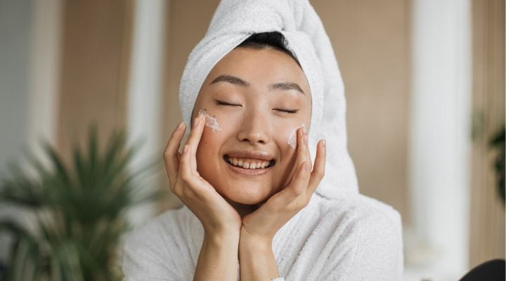 Foto de uma modelo aplicando creme facial em seu momento de skincare.