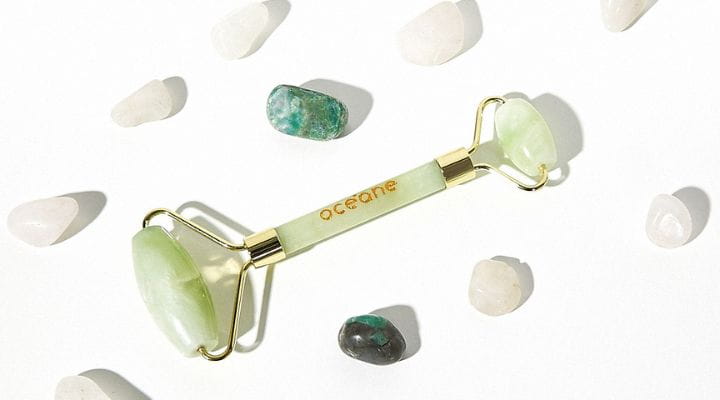 Foto do massageador jade roller da Océane no centro e em volta algumas pedras de jade verde.