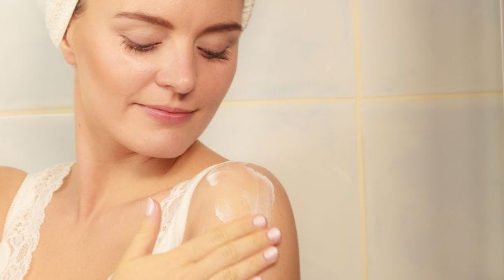Foto de uma modelo aplicando um creme hidratante corporal no braço.