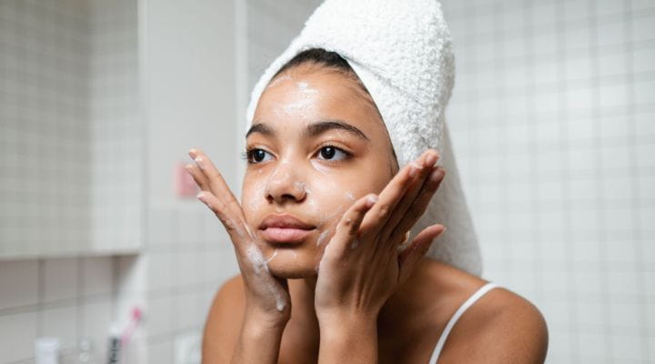 Foto de uma menina lavando o rosto em sua rotina de skincare olhando para o espelho.