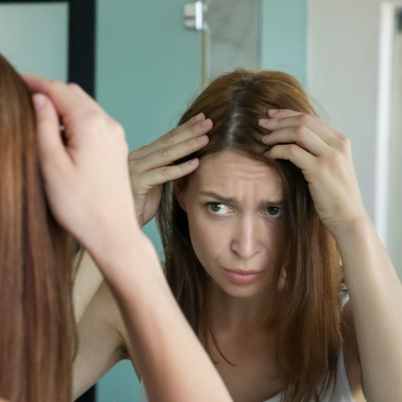 modelo olhando para o espelho preocupada com a queda de cabelo