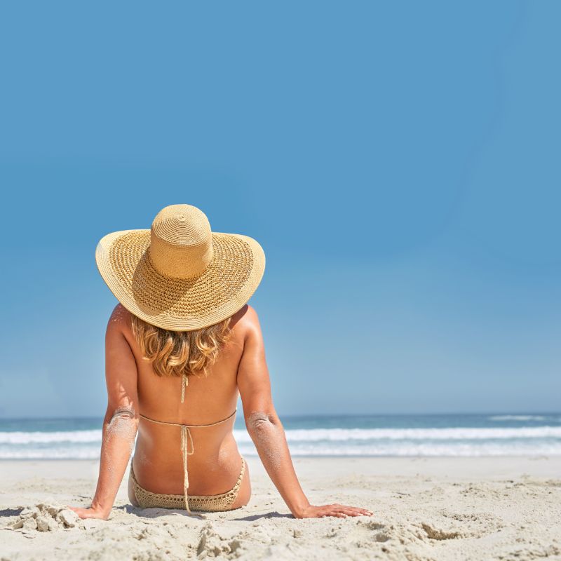 mulher olhando o mar, sentada na areia.