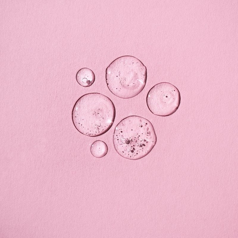 gotas de líquido rico em peptídeos sobre um fundo rosa de texturas