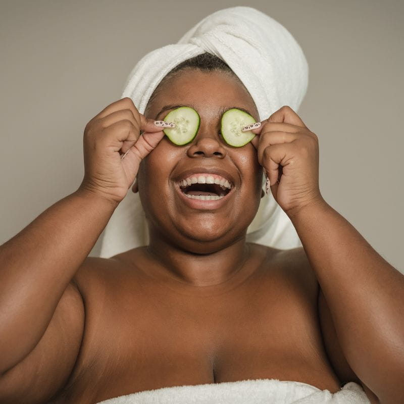 Modelo realizando um spa day com pepinos nos olhos e toalha na cabeça.