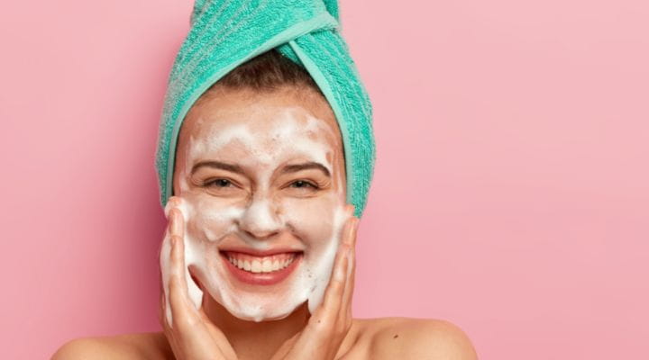 mulher limpando a pele com gel de limpeza facial e está com bastante espuma no rosto