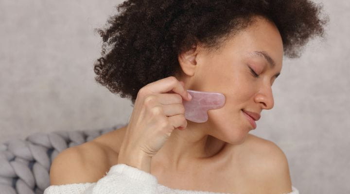 modelo massageando o rosto com pedra de quartzo rosa 