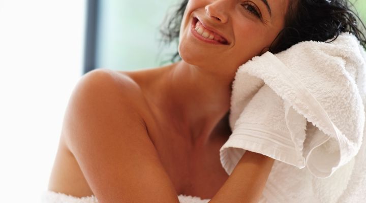 Mulher sorridente secando cabelo com toalha branca.