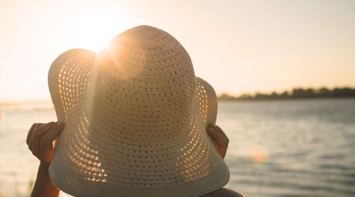 Mulher segurando chapéu ao pôr do sol próximo a água