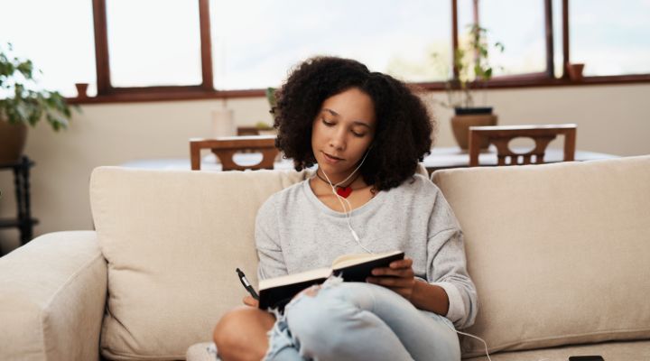 Jovem lendo livro com fones de ouvido no sofá