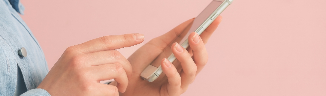 Mão segurando smartphone em fundo rosa