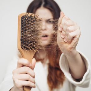 Mulher segura escova de cabelo com uma mão e puxa fios da escova com outra.