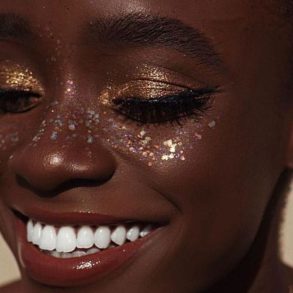 modelo sorridente com maquiagem de carnaval dourada e cheia de glitter