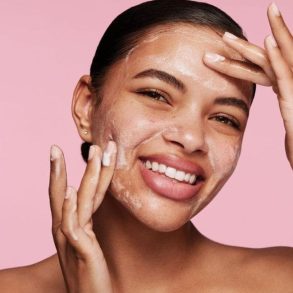 Modelo sorridente passando esfoliante facial na testa e na bochecha