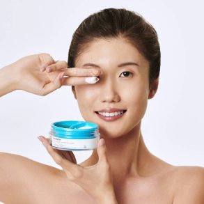 Mulher sorrindo aplicando creme Océane na área dos olhos.